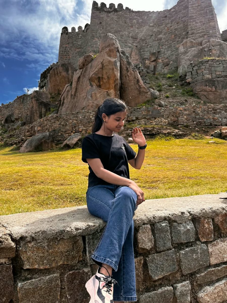Bhargavi sitting on a stone wall in front of an old fort