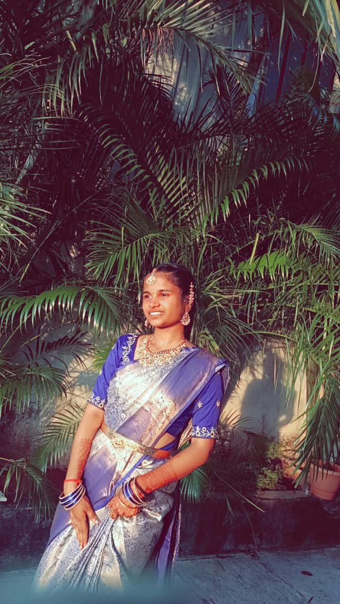 Bhargavi in a blue silk saree standing in front of palm leaves