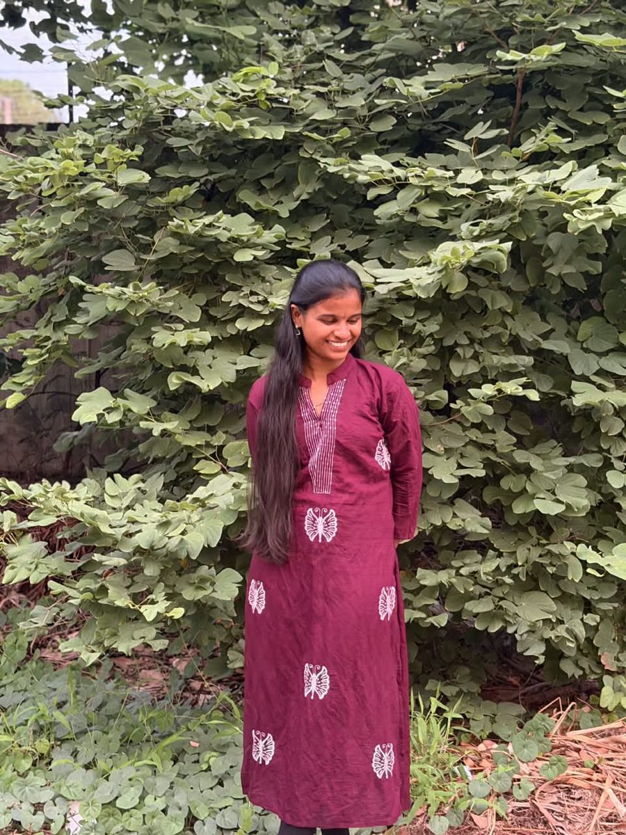 Bhargavi smiling in a maroon kurti with butterflies, standing in a garden